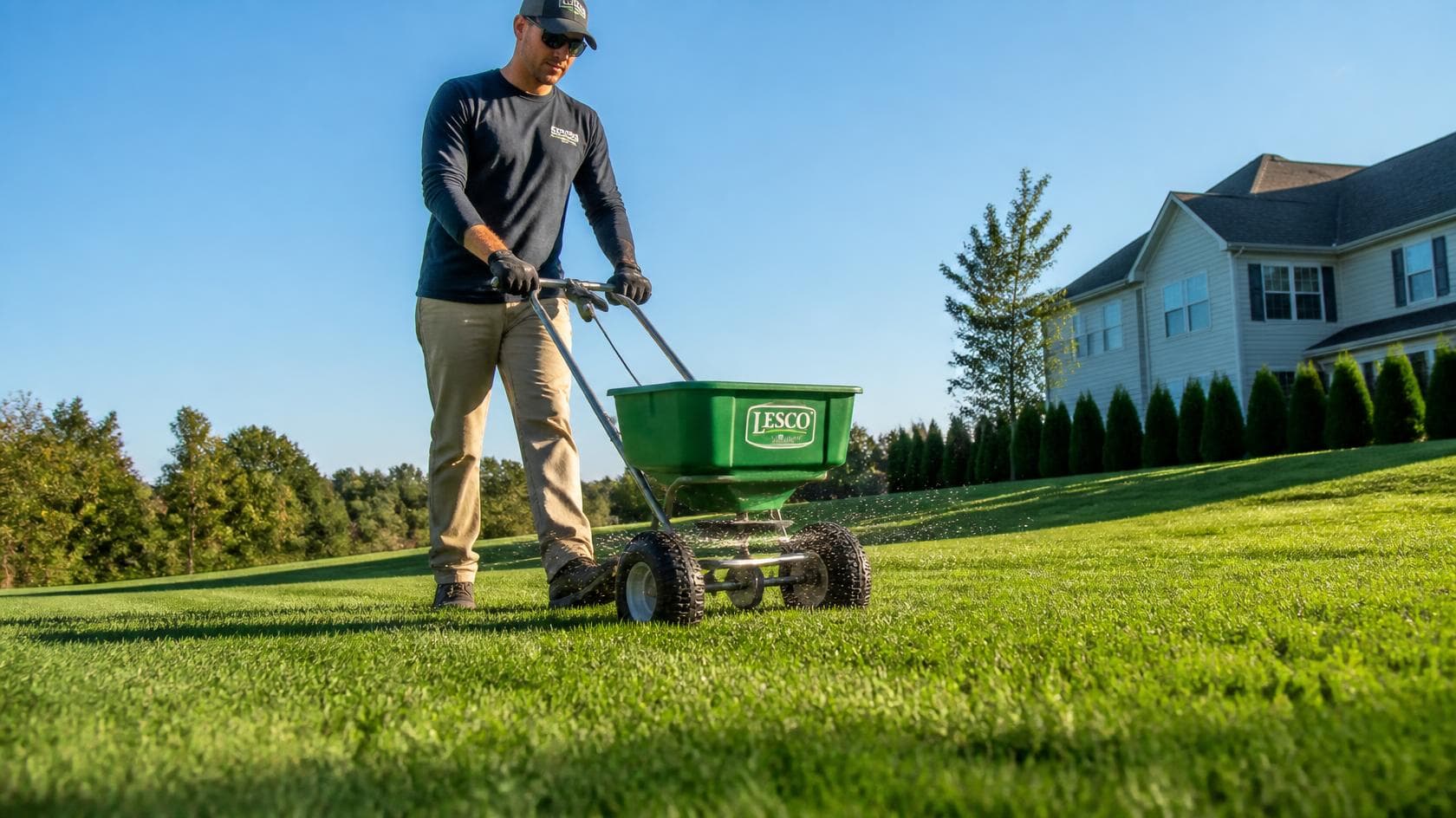 Lawn care professional seeding a residential lawn with a push spreader